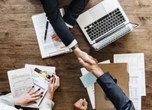 2 personnes se serrent la main à une table de travail pendant qu'une troisième prend des notes. Vue de dessus