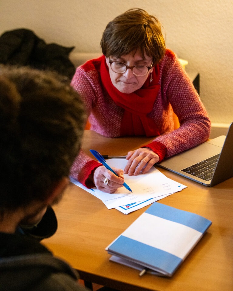 Une formatrice accompagne une personne lors d'un entretien individuel. Assise à un bureau, elle montre un document et prend des notes, avec un ordinateur portable ouvert à ses côtés.